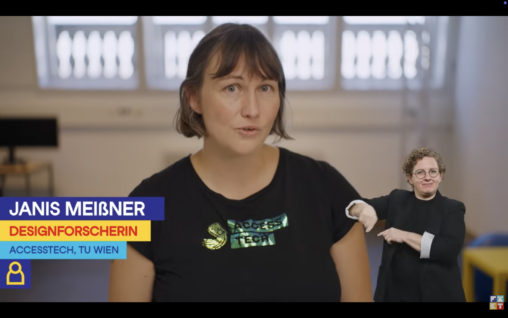 Video still. A label introduces Janis as a design researcher in the ACCESSTECH project at TU Wien. A sign language interpreter is displayed in the right bottom corner to translate.